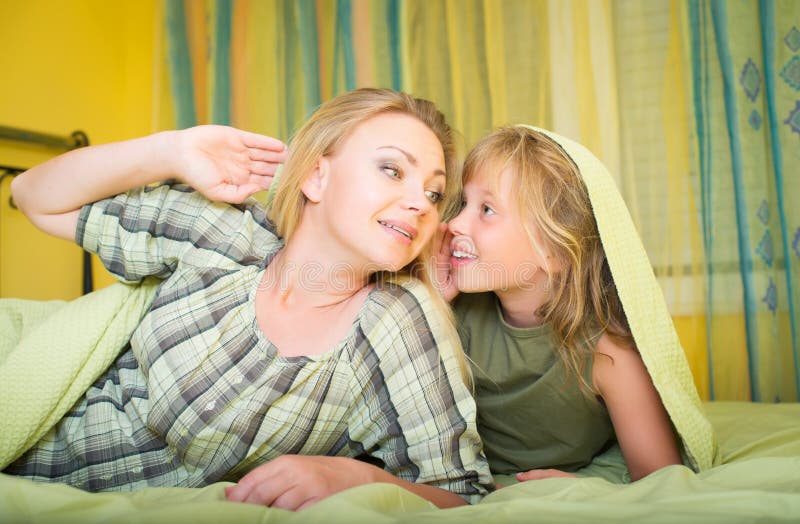 Madre e piccola figlia che si trovano a letto e che parlano famiglia bedtime fotografia stock Madre e piccola figlia che si trovano a letto e che parlano famiglia bedtime fotografia stock