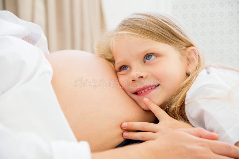 Madre embarazada sonriente feliz que abraza con su hija en casa foto de archivo Madre embarazada sonriente feliz que abraza con su hija en casa foto de archivo