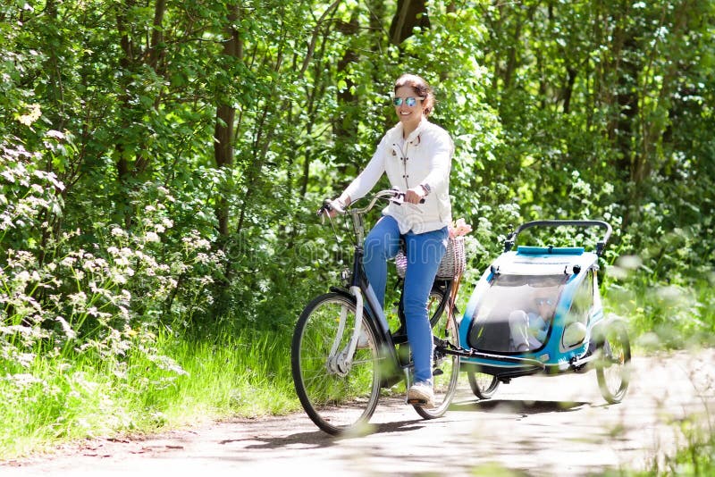 Madre en la bicicleta con el remolque de la bici del bebé en parque fotografía de archivo libre de regalías Madre en la bicicleta con el remolque de la bici del bebé en parque fotografía de archivo libre de regalías