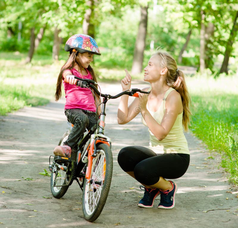 Madre felice che parla con sua figlia che sorride, che insegna a al ciclismo immagini stock libere da diritti Madre felice che parla con sua figlia che sorride, che insegna a al ciclismo immagini stock libere da diritti