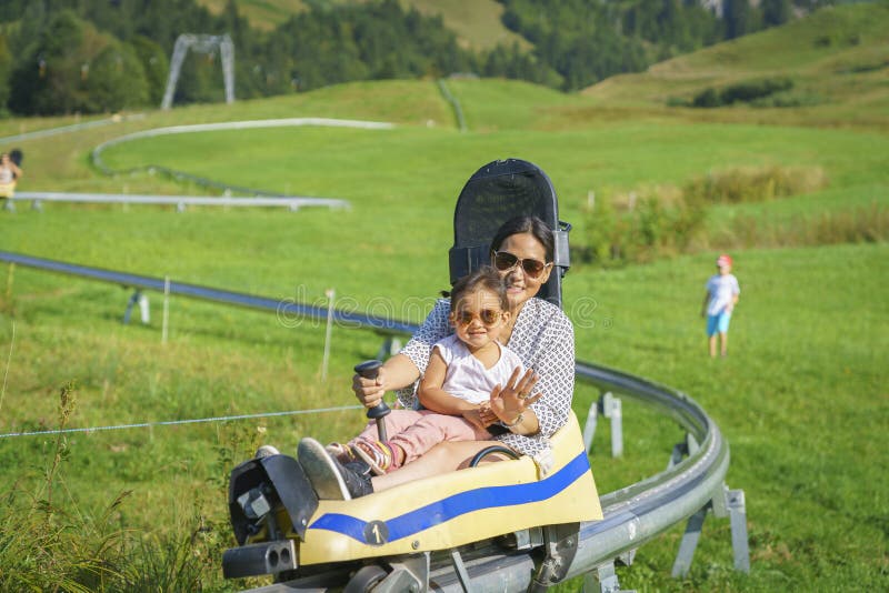 Madre felice della famiglia e figlia del bambino piccola nel toboggan di estate immagine stock Madre felice della famiglia e figlia del bambino piccola nel toboggan di estate immagine stock