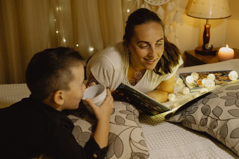 Madre felice e ragazzo che leggono un libro a letto prima dell'andare a dormire immagine stock libera da diritti Madre felice e ragazzo che leggono un libro a letto prima dell'andare a dormire immagine stock libera da diritti