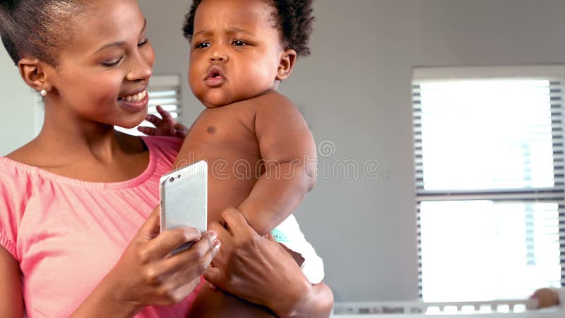 Madre feliz con el teléfono que levanta a su bebé