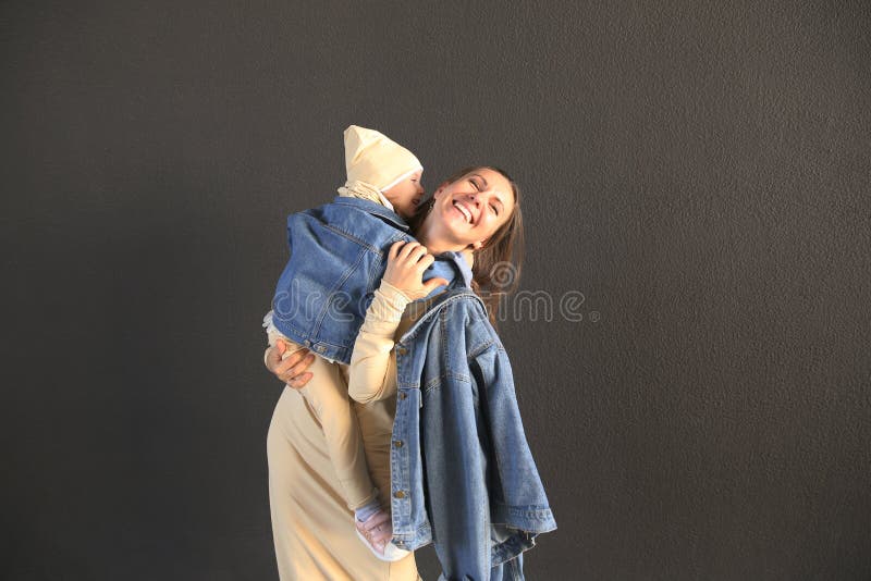 Madre feliz que abraza a su bebé en ropa elegante en un fondo gris fotografía de archivo libre de regalías Madre feliz que abraza a su bebé en ropa elegante en un fondo gris fotografía de archivo libre de regalías
