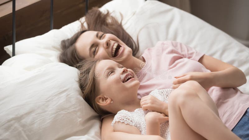 Madre graziosa e figlia che si trovano a letto ridendo divertendosi immagine stock libera da diritti Madre graziosa e figlia che si trovano a letto ridendo divertendosi immagine stock libera da diritti