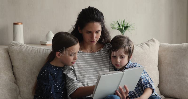 Madre hispana joven leyendo libros de papel a niños pequeños. almacen de video