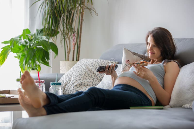 Madre incinta dei giovani, mangiando pizza saporita a casa, guardando TV fotografie stock libere da diritti Madre incinta dei giovani, mangiando pizza saporita a casa, guardando TV fotografie stock libere da diritti