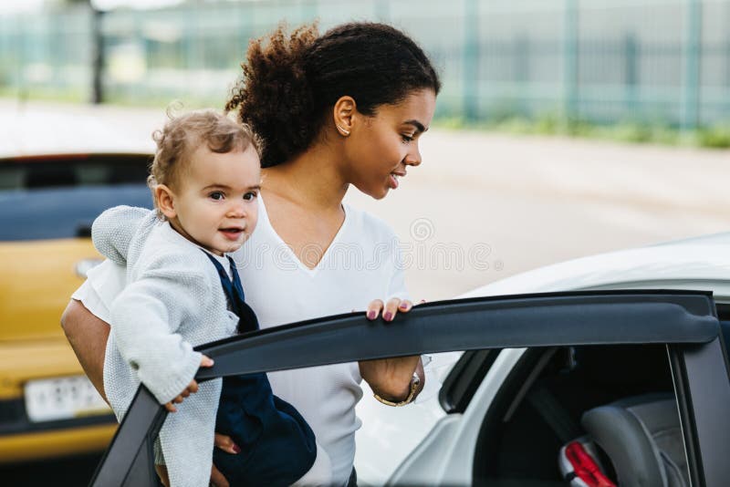 Madre joven abriendo una puerta de auto sostiene a una hija pequeña fotos de archivo libres de regalías