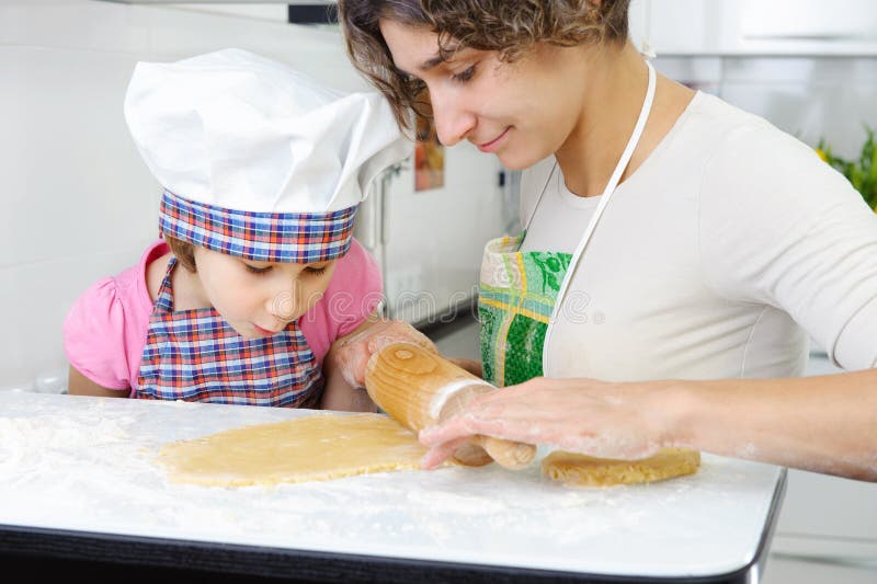 Madre joven con la pequeña hija que prepara las galletas foto de archivo Madre joven con la pequeña hija que prepara las galletas foto de archivo