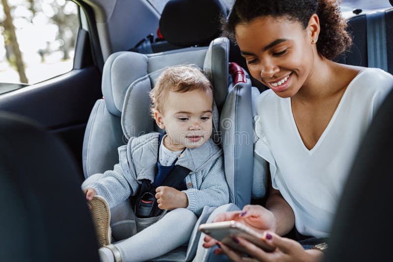 Madre joven con su hija sentada en el asiento trasero de un auto Mujer y una niña pequeña mirando el celular en el auto