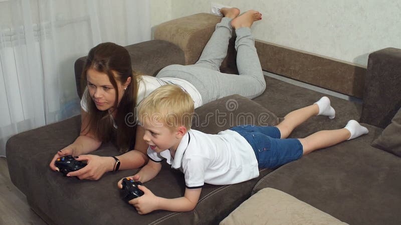 Madre joven con un hijo pequeño jugando a juegos de computadora en el sofá en casa almacen de video