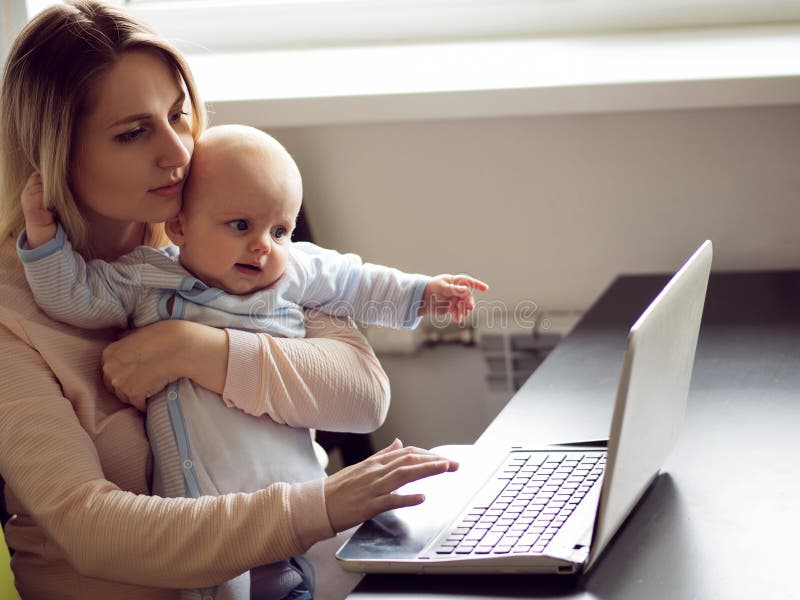 Young mother in home office with computer and her baby. Work and child care. Young mother in home office with computer and her baby. Work and child care