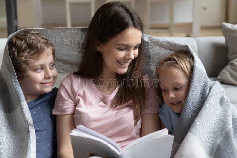 Madre joven leyendo cuento de hadas a niños adorables fotos de archivo
