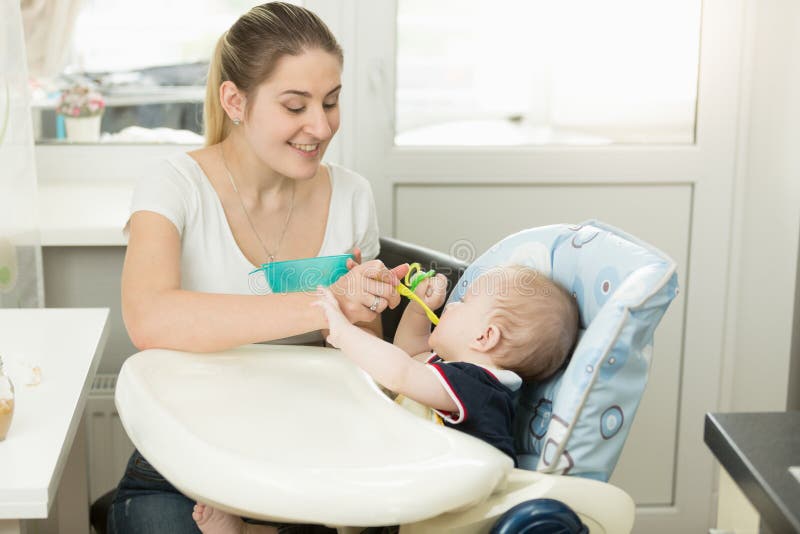 Madre joven sonriente que alimenta a su bebé en highchair fotografía de archivo Madre joven sonriente que alimenta a su bebé en highchair fotografía de archivo