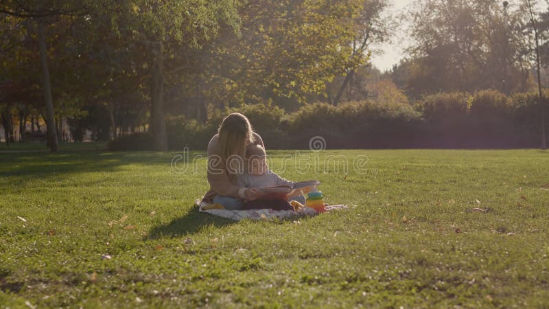 Madre leyendo un libro a su hijo en un parque almacen de video