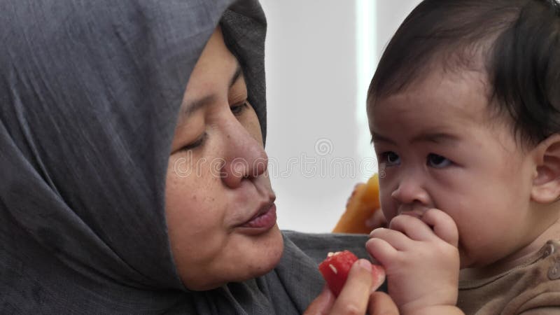 Madre musulmana asiática alimenta a su bebé con frutas frescas almacen de video