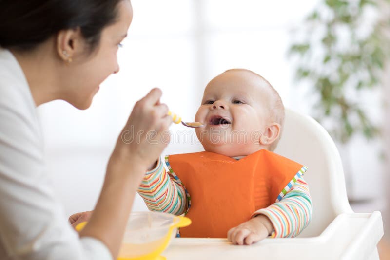 Madre que alimenta a su bebé con la cuchara Mime a dar la comida sana a su niño adorable en casa