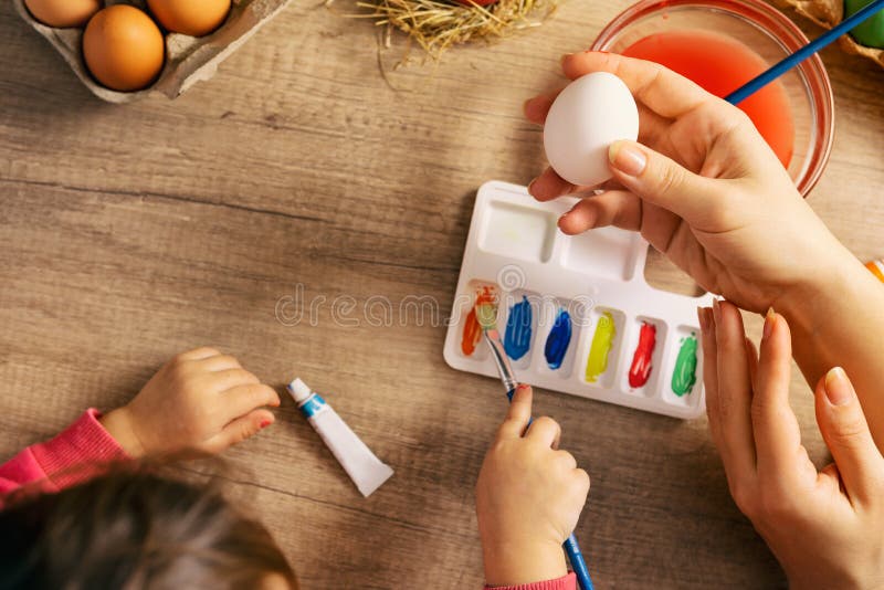 Madre que ayuda a su pequeña hija a pintar el huevo de Pascua imagenes de archivo Madre que ayuda a su pequeña hija a pintar el huevo de Pascua imagenes de archivo