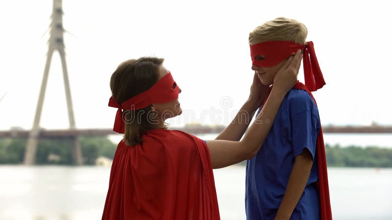 Madre que cuida en el traje del super héroe que mira con amor el hijo, orgulloso de su niño imagenes de archivo Madre que cuida en el traje del super héroe que mira con amor el hijo, orgulloso de su niño imagenes de archivo