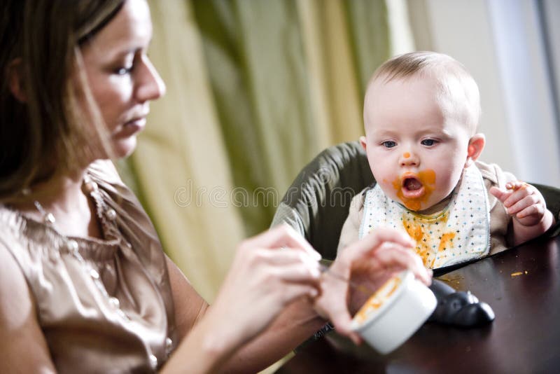 Madre que introduce el alimento hambriento del sólido del bebé imagen de archivo libre de regalías Madre que introduce el alimento hambriento del sólido del bebé imagen de archivo libre de regalías