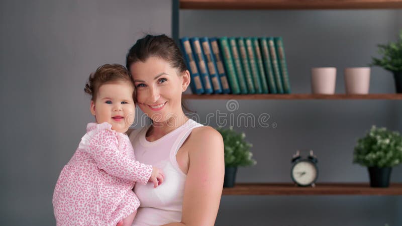 Madre que recibe a una hija recién nacida cerca de una estantería que irradia una conexión cálida y sensibilidad materna durante e almacen de metraje de vídeo