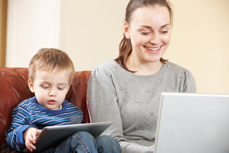 Madre que trabaja en el ordenador portátil mientras que el hijo utiliza la tableta de Digitaces fotografía de archivo libre de regalías Madre que trabaja en el ordenador portátil mientras que el hijo utiliza la tableta de Digitaces fotografía de archivo libre de regalías