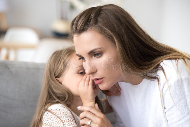 Madre seria de amor que escucha la muchacha del niño que susurra en oído fotografía de archivo Madre seria de amor que escucha la muchacha del niño que susurra en oído fotografía de archivo