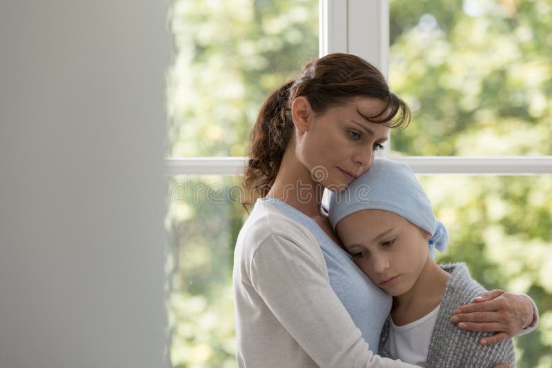 Madre triste che abbraccia figlia malata con cancro che indossa foulard blu