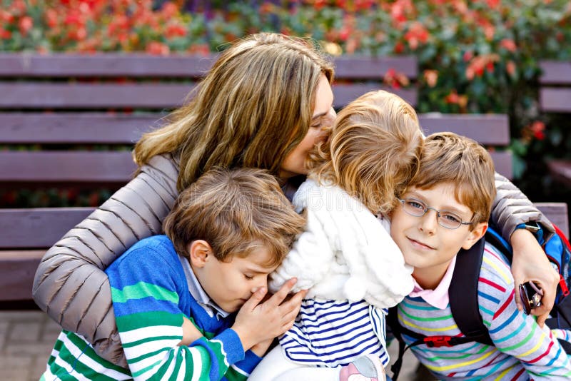 Madre y abrazo de tres niños El sentarse feliz de la familia al aire libre: mujer y dos niños del muchacho de los niños del herma imagenes de archivo