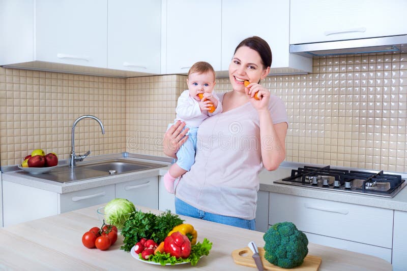 Madre y bebé que comen la zanahoria en la cocina imagen de archivo Madre y bebé que comen la zanahoria en la cocina imagen de archivo