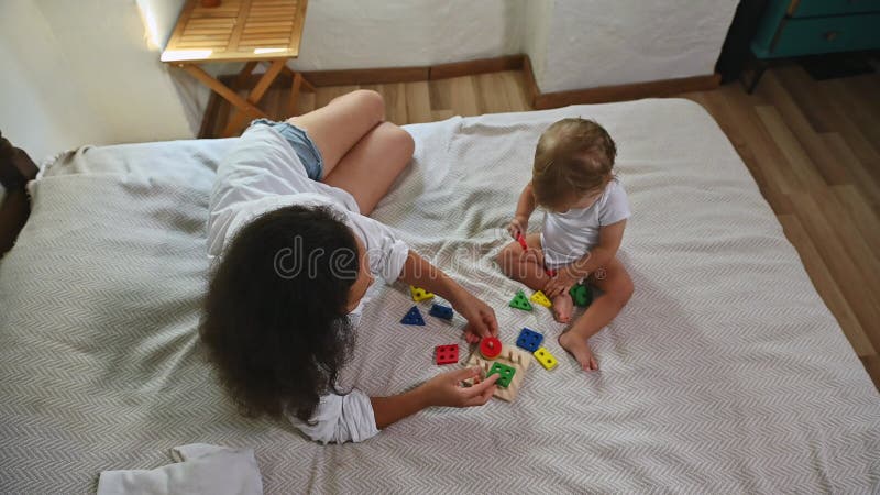 Madre y niño jugando con coloridos juguetes educativos en una cómoda cama metrajes
