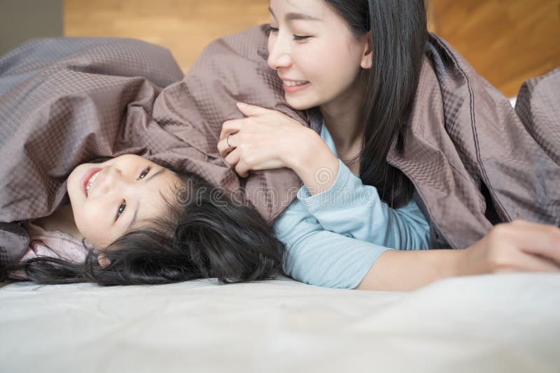 Madre y su muchacha del niño de la hija que juegan en el dormitorio y que ponen la manta Familia asi?tica feliz foto de archivo libre de regalías Madre y su muchacha del niño de la hija que juegan en el dormitorio y que ponen la manta Familia asi?tica feliz foto de archivo libre de regalías