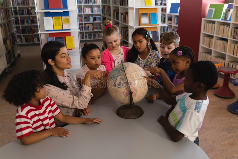 Maestra que enseña a los niños sobre el globo en la tabla en biblioteca escolar imagenes de archivo Maestra que enseña a los niños sobre el globo en la tabla en biblioteca escolar imagenes de archivo