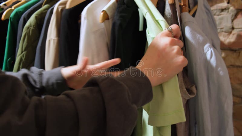 Magasin secondaire. Closeup de la jeune femme les mains surfer les vêtements sur les cintres. banque de vidéos