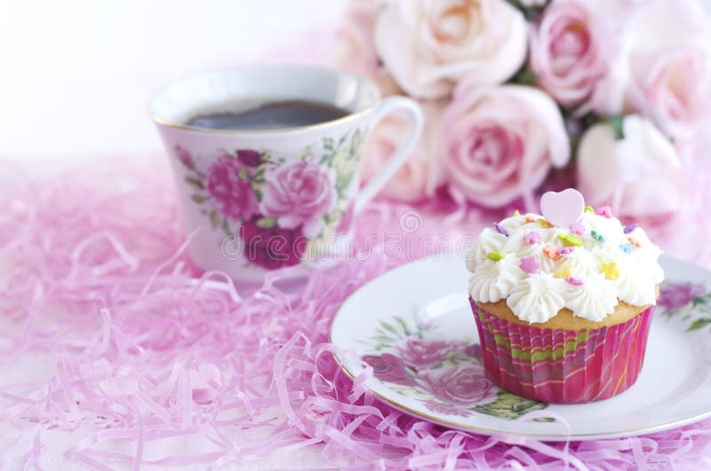 A pretty decorated cupcake with sprinkles and pink candy heart, with cup of coffee. A pretty decorated cupcake with sprinkles and pink candy heart, with cup of coffee