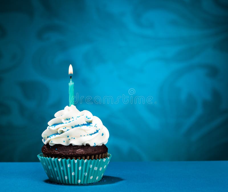 Chocolate Cupcake with icing and lit birthday candle over a blue background. Chocolate Cupcake with icing and lit birthday candle over a blue background