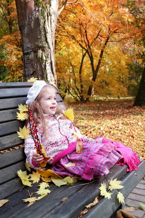 Una bambina seduta disegnata in piedi su una panchina, in autunno, parco, tenendo in mano rami di crespino e guardando con ammirazione degli alberi circostanti.