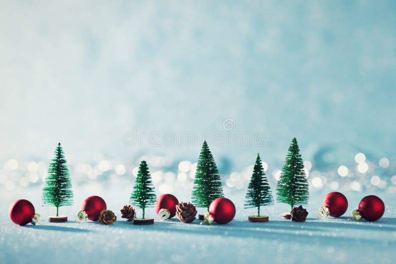 Magical miniature winter wonderland background. Evergreen trees, pine cones and red christmas baubles on shiny blue background with bokeh in the background. Magical miniature winter wonderland background. Evergreen trees, pine cones and red christmas baubles on shiny blue background with bokeh in the background.