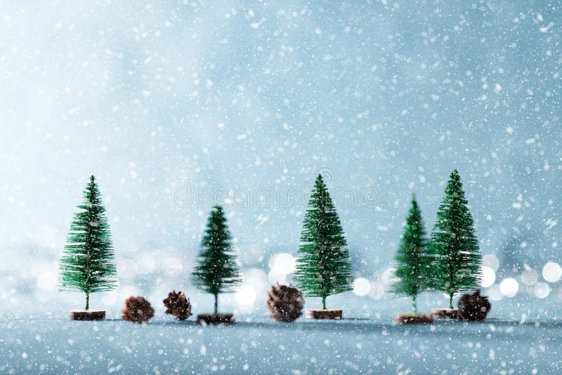 Magical snowy winter wonderland background. Miniature evergreen trees and pine cones on shiny blue background with bokeh in the background.