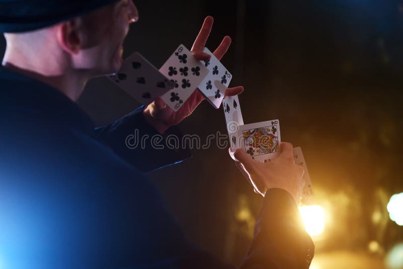 Magician showing trick with playing cards. Magic or dexterity, circus, gambling. Prestidigitator in dark room with fog stock photo Magician showing trick with playing cards. Magic or dexterity, circus, gambling. Prestidigitator in dark room with fog stock photo