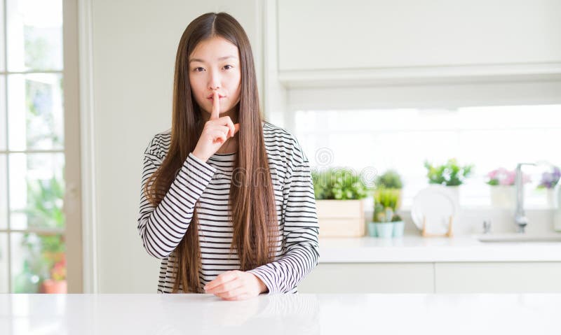 Maglione d'uso delle bande della bella donna asiatica che chiede di fare silenzio con il dito sulle labbra fotografia stock