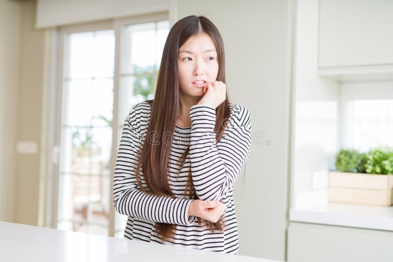 Maglione d'uso delle bande della bella donna asiatica che sembra sottolineato e nervoso con le mani sulle unghie mordenti della bo fotografie stock