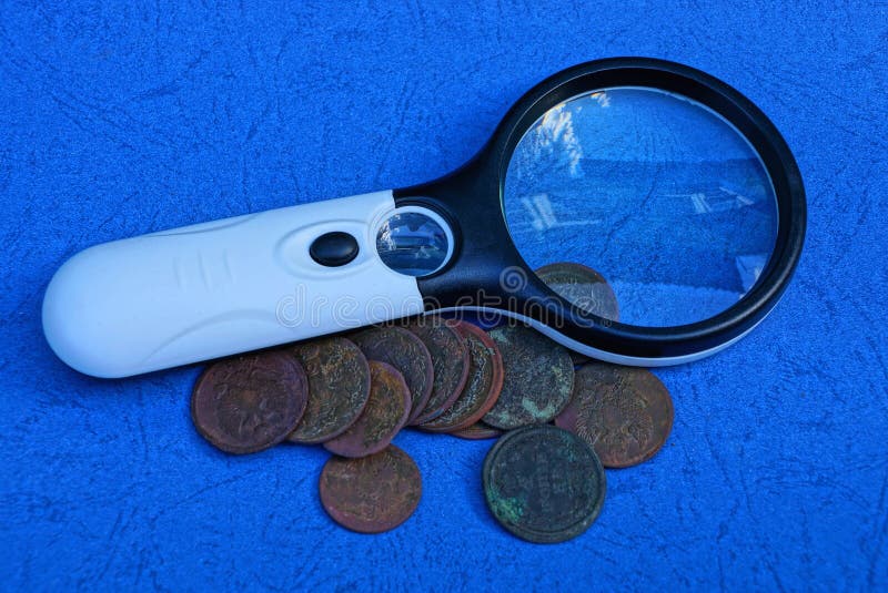 Magnifier and a Bunch of Old Copper Coins on a Blue Table Stock Photo