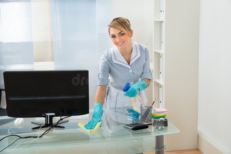 Maid cleaning desk in office royalty free stock photography