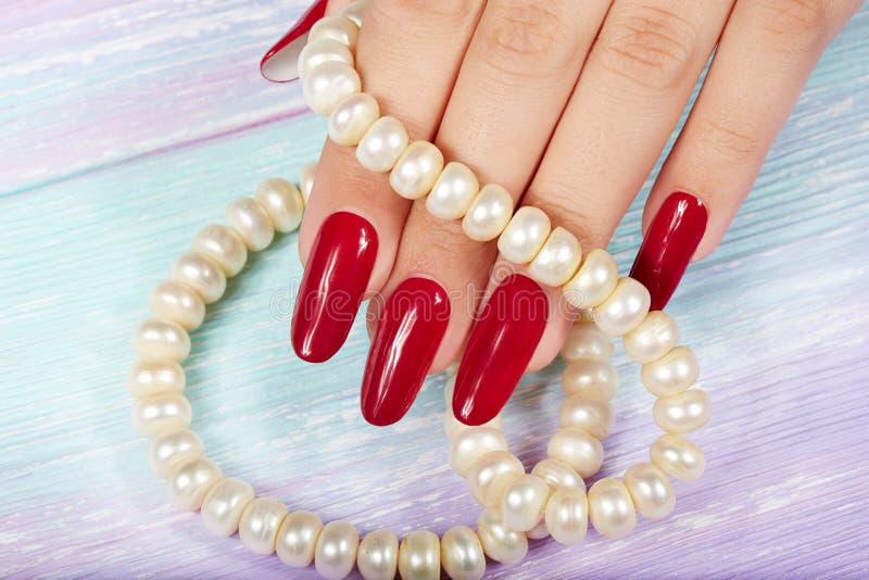 Hand with long artificial manicured nails colored with red nail polish and a necklace. Hand with long artificial manicured nails colored with red nail polish and a necklace