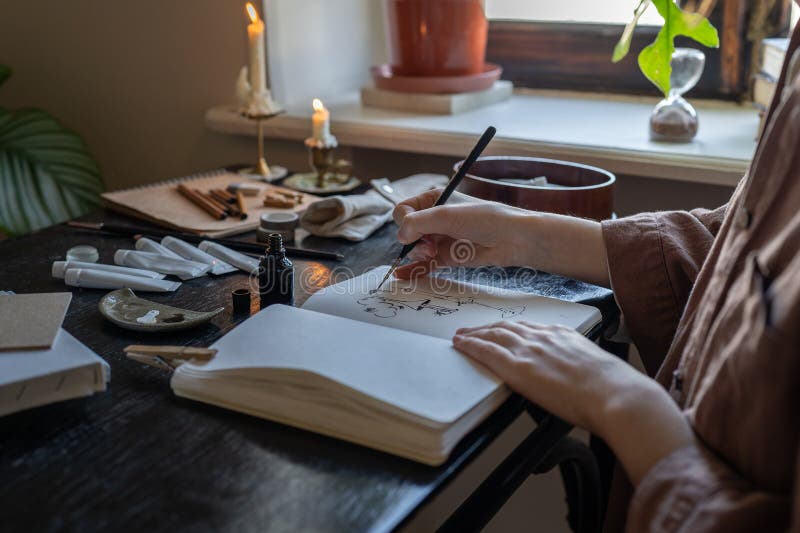 Main d'artiste féminine avec pinceau fine créer un croquis dans bloc-notes dans l'atmosphère romantique. travail de confort photo libre de droits