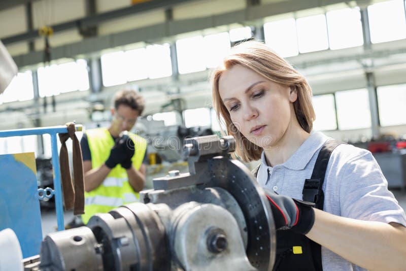 Main-d'œuvre féminine mûr travaillant aux machines avec le collègue à l'arrière-plan à l'industrie images stock Main-d'œuvre féminine mûr travaillant aux machines avec le collègue à l'arrière-plan à l'industrie images stock