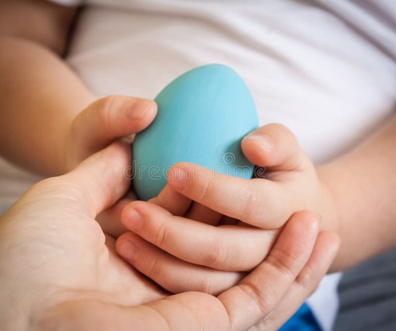 Main de bébé tenant l'oeuf bleu dans la main de mère, plan rapproché photo stock Main de bébé tenant l'oeuf bleu dans la main de mère, plan rapproché photo stock