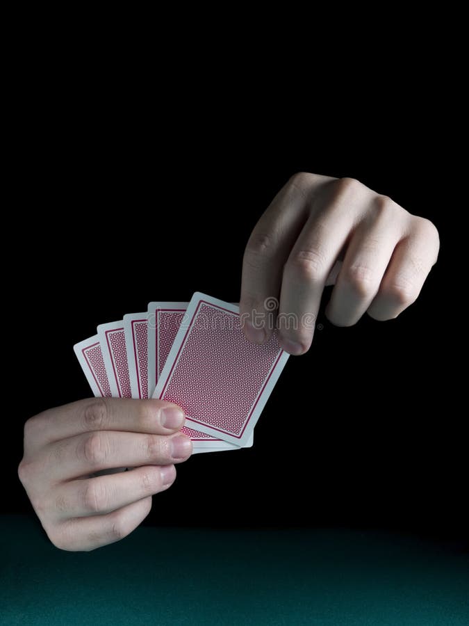 A man's hand holding five cards over a green felt. A man's hand holding five cards over a green felt.