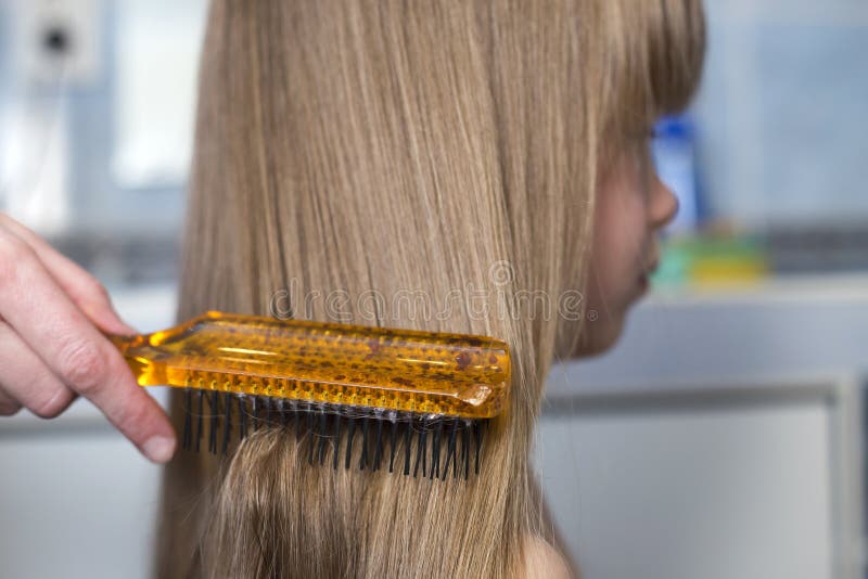 Main de mère avec la brosse peignant de longs cheveux justes de fille mignonne d'enfant sur le fond intérieur brouillé Verticale images stock Main de mère avec la brosse peignant de longs cheveux justes de fille mignonne d'enfant sur le fond intérieur brouillé Verticale images stock
